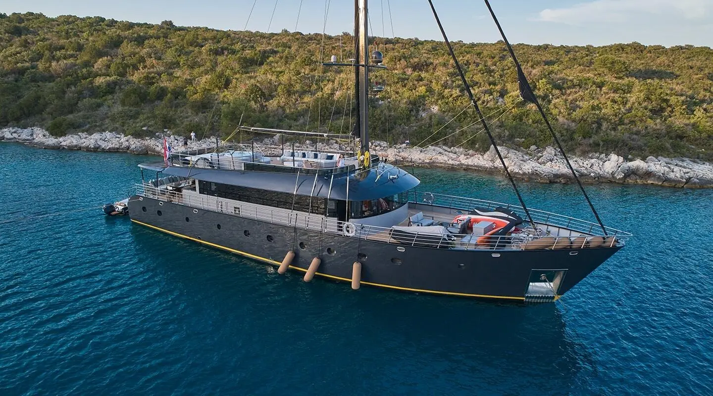 Blue luxury gulet yacht named Rara Avis anchored near rocky coastline at sunset