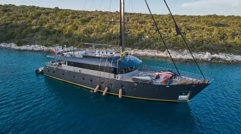 Blue luxury gulet yacht named Rara Avis anchored near rocky coastline at sunset