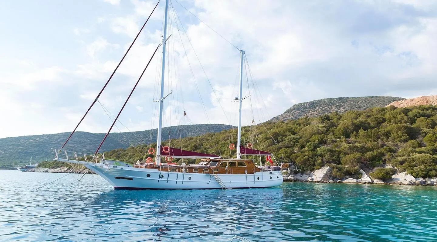 Primadonna yacht anchored near a cliffy coastline at sunset with masts and calm blue waters