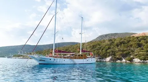 Primadonna yacht anchored near a cliffy coastline at sunset with masts and calm blue waters