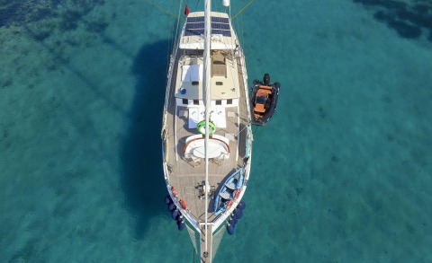 Gazella sailing yacht from above, teak deck lounge area and dinghy secured to starboard, turquoise sea
