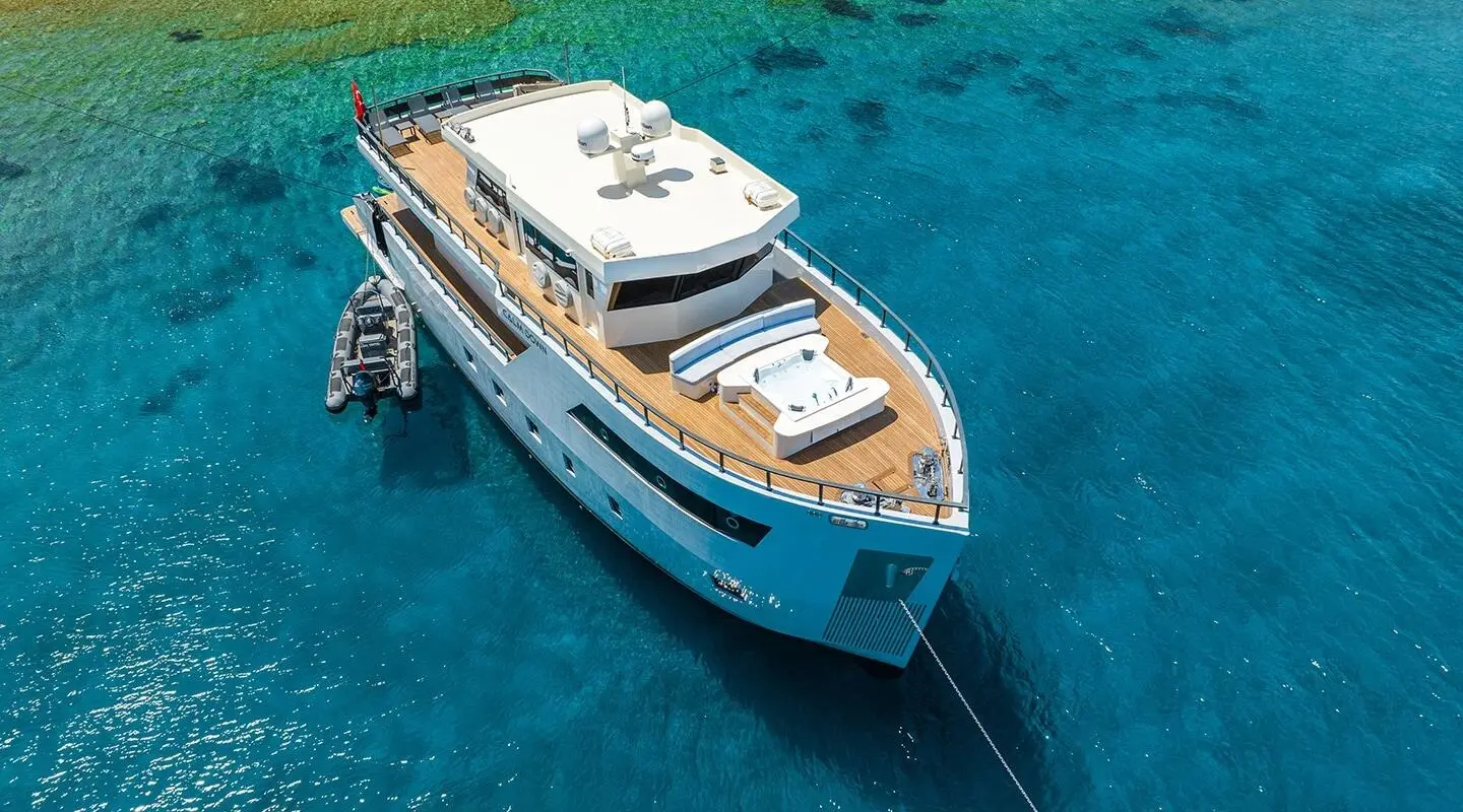 A blue motor yacht Calm Down anchored in clear turquoise water from above