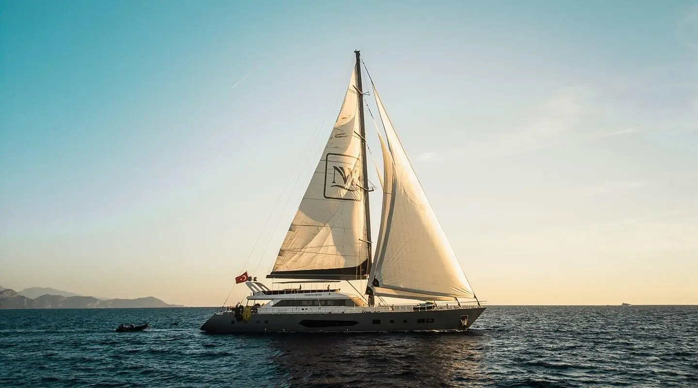 Sailing yacht on open sea with tall sails at sunset