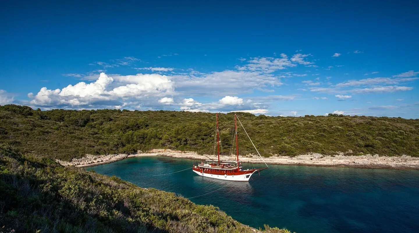 Romanca yacht anchored in a clear cove with rocky shore and blue water