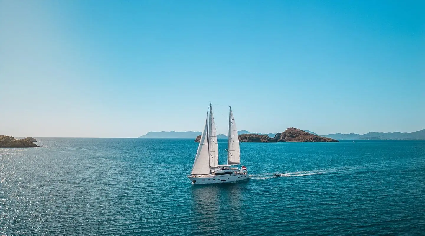 Angelo III sailing yacht on blue sea, white sails raised, cruising near small rocky islets