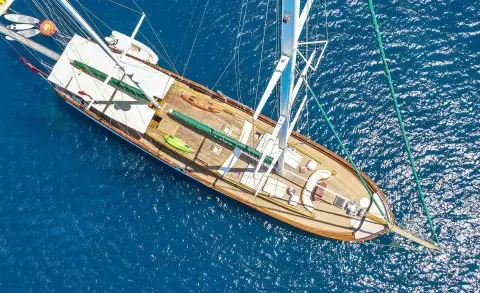Top-down view of a wooden luxury yacht with sails at sunset on blue water