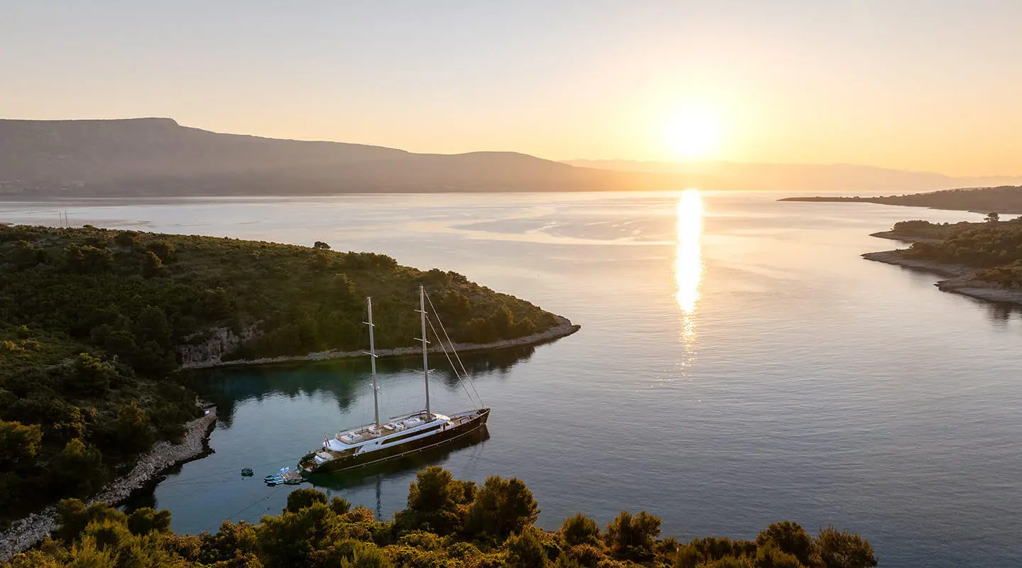 Nocturno yacht anchored near rocky coastline at sunset over calm sea