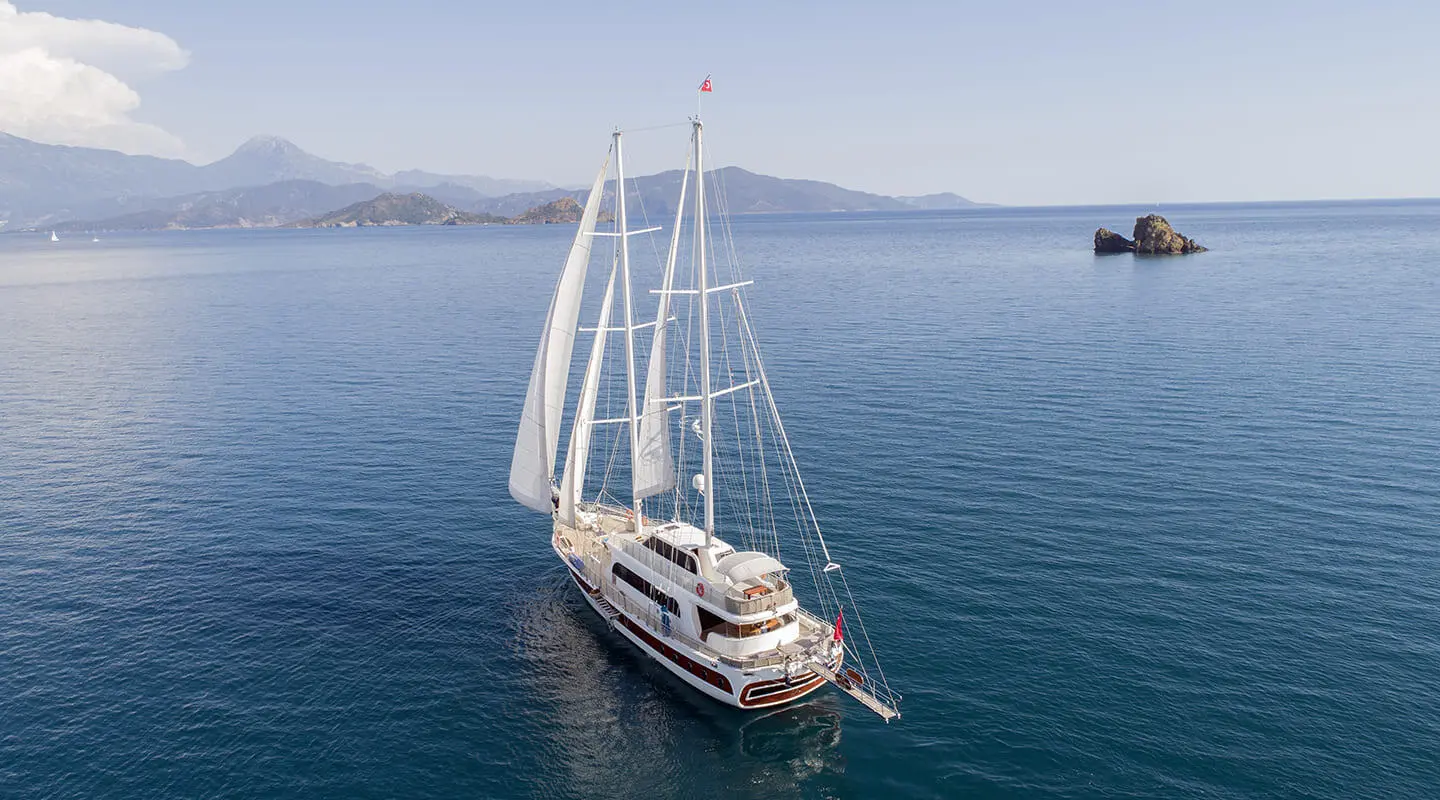 Kayhan 4 luxury gulet sailing at sunset with tall masts on calm blue sea