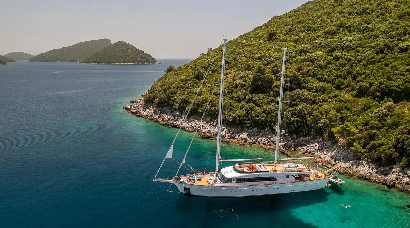 Gulet Love Story anchored near a rocky hillside with clear blue water