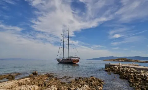 Wooden sailing yacht anchored near rocky shore under a blue sky