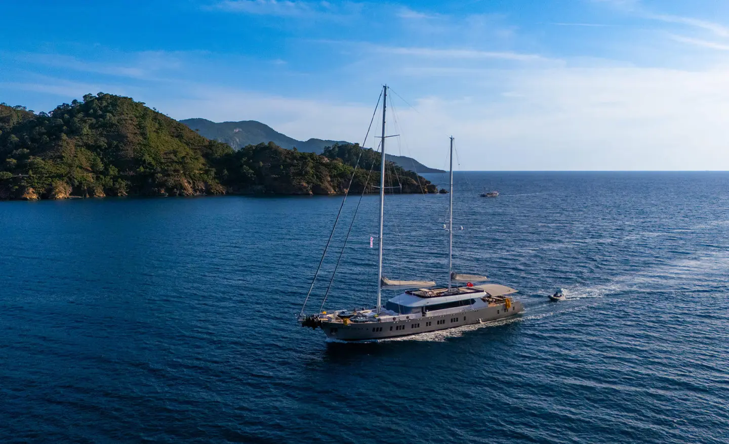 Two-masted modern yacht sailing on calm blue sea near coastline