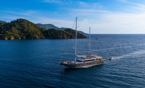 Two-masted modern yacht sailing on calm blue sea near coastline
