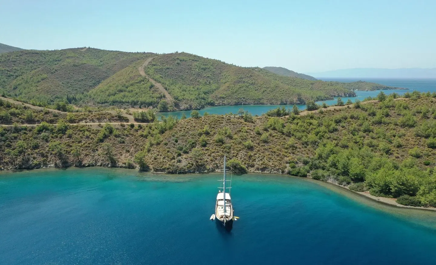Enderim A yacht anchored near green hills with a small boat nearby