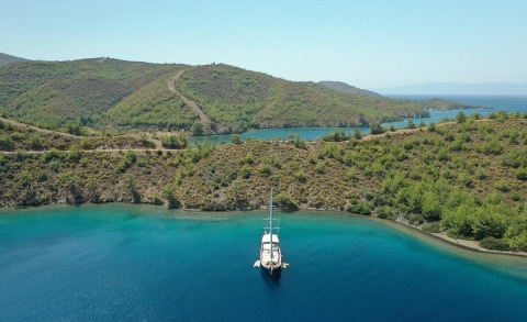 Enderim A anchored in a turquoise bay, surrounded by rugged green hills and clear blue water