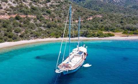 Ulucinar sailing yacht anchored near a turquoise cove with a sandy beach and green hills
