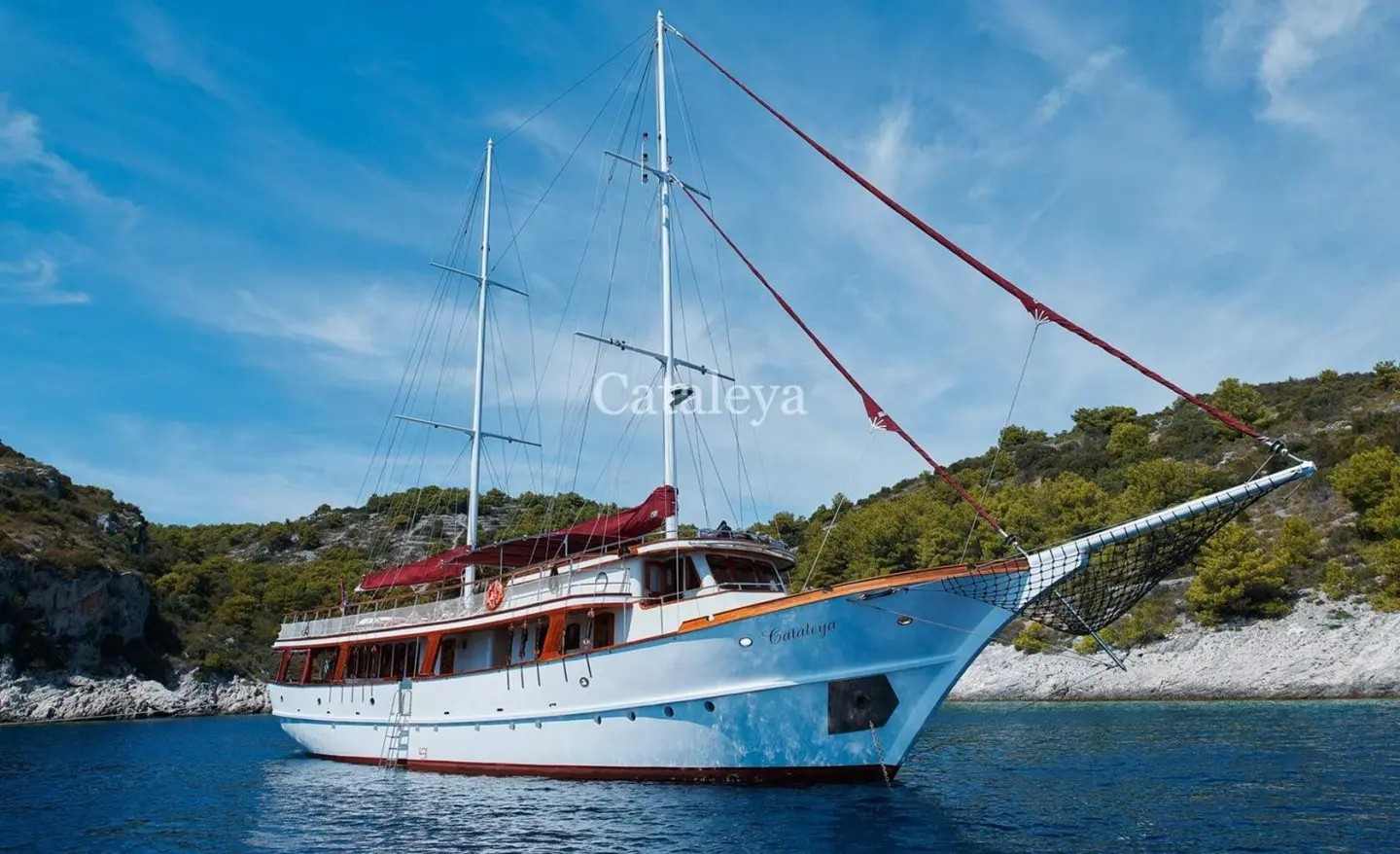 Cataleya yacht anchored near rocky coastline at sunset with blue sky