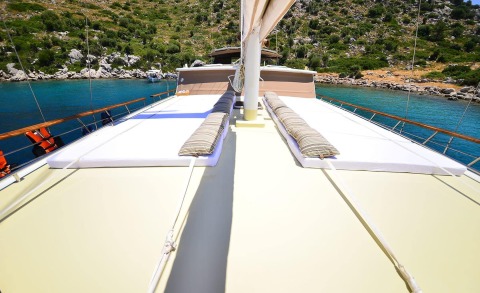View from Prenses Bugce gulet sun deck with striped cushions and blue water by rocky shoreline