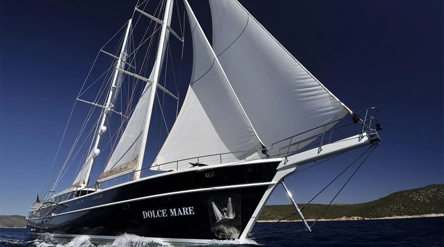 Dolce Mare yacht sails with dark hull and white sails in blue sea