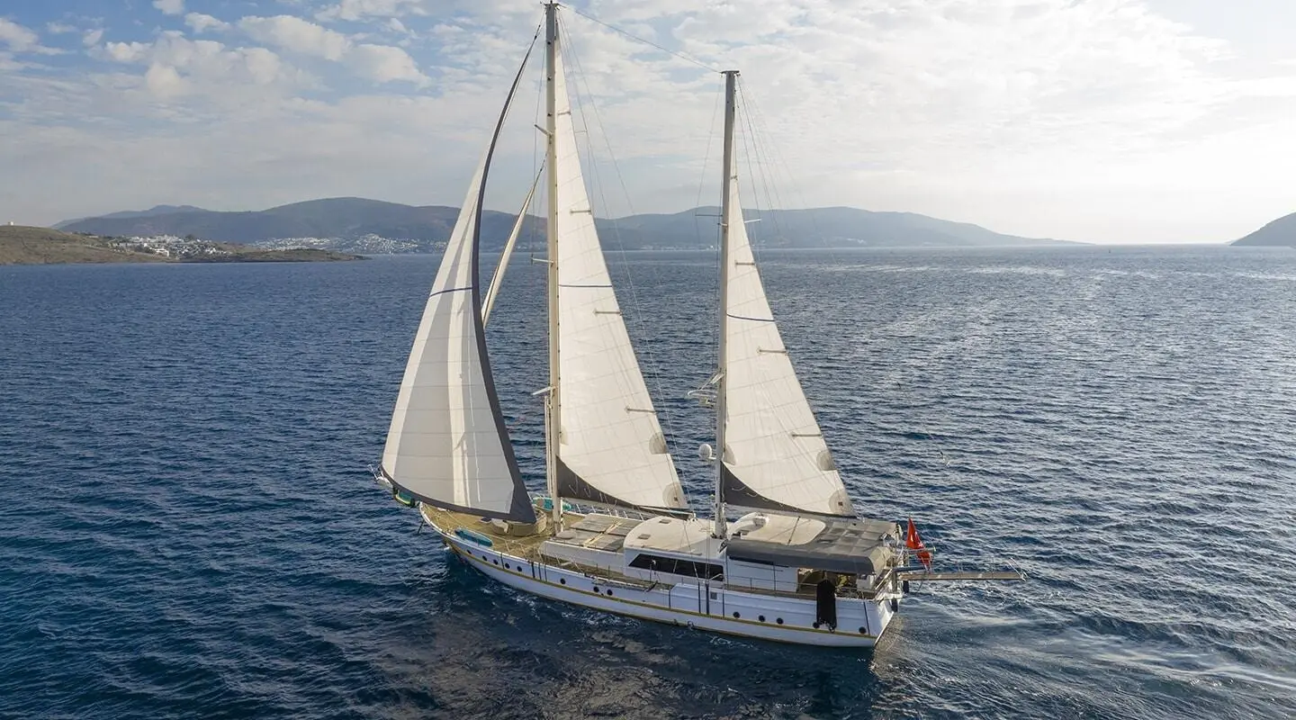 Two-masted sailing yacht on open sea with distant coastline in the background