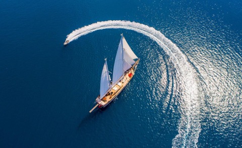 A three-masted gulet sailing boat in open sea with sails up, leaving a wake behind on blue water