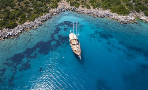 Wooden sailing yacht anchored in turquoise blue water near rocky shoreline