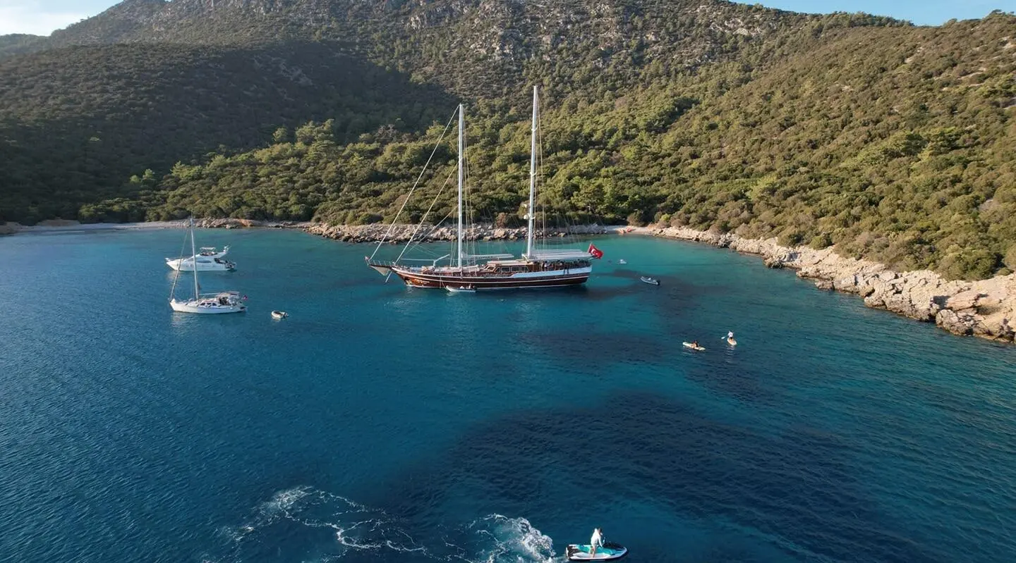 Large sailing yacht anchored in turquoise water bay with small boats nearby