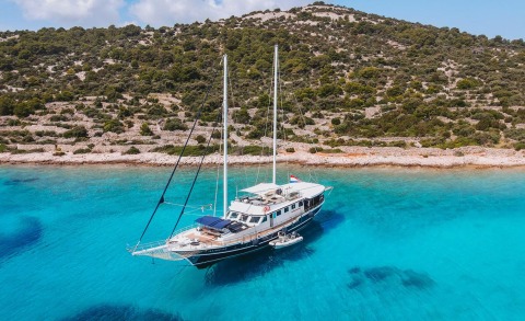 Aurum luxury sailing yacht anchored in turquoise lagoon beside rocky hillside
