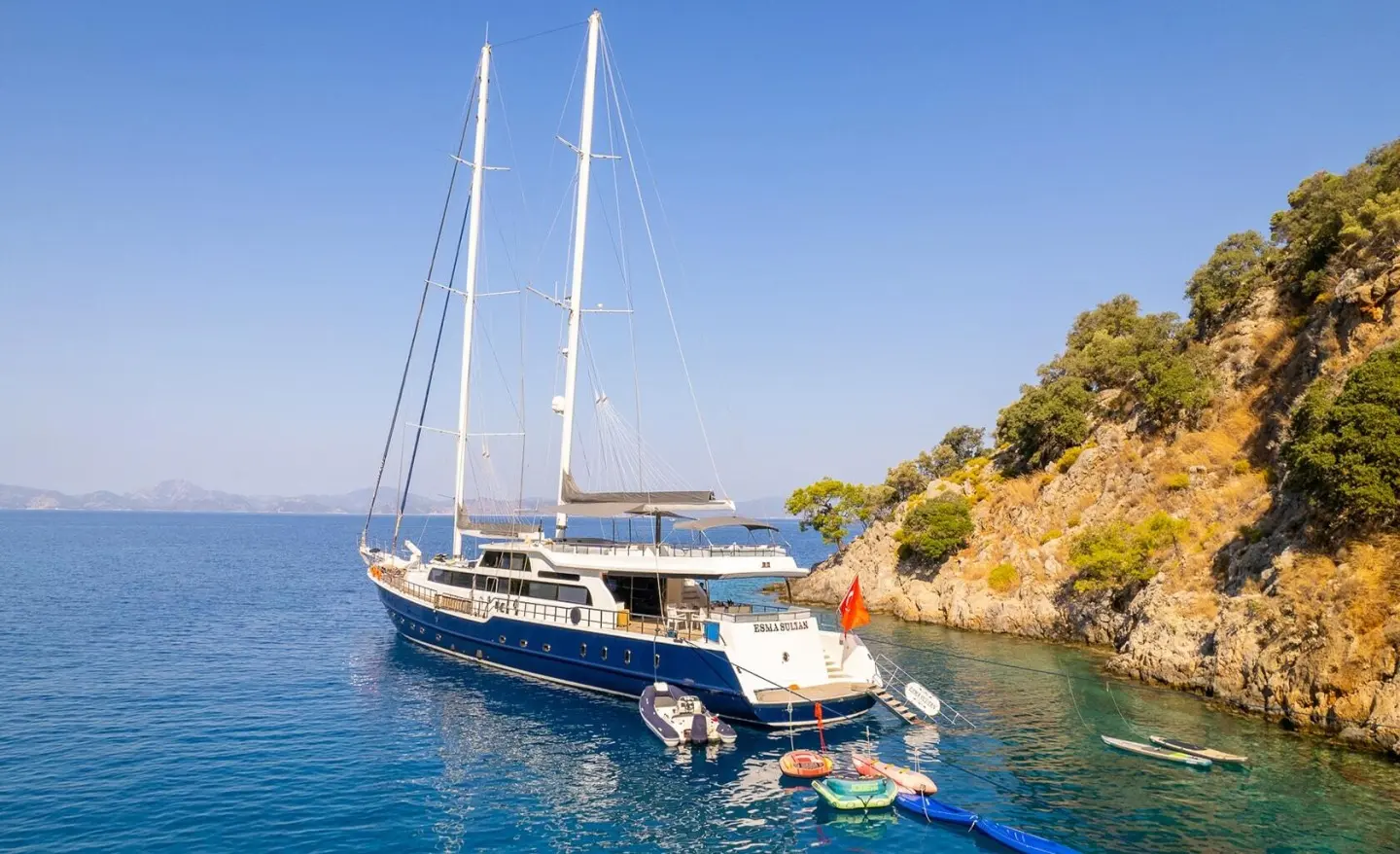 Esma Sultan luxury sailing yacht anchored near rocky coastline with clear blue sea