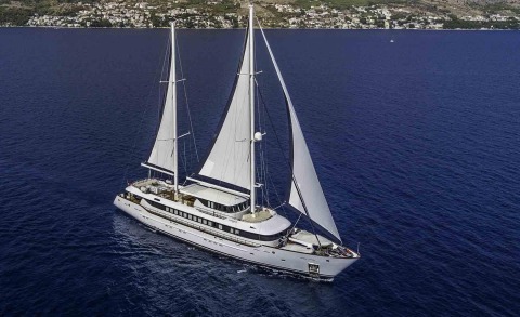 Omnia sailing yacht with two masts gliding in clear blue sea near coastline