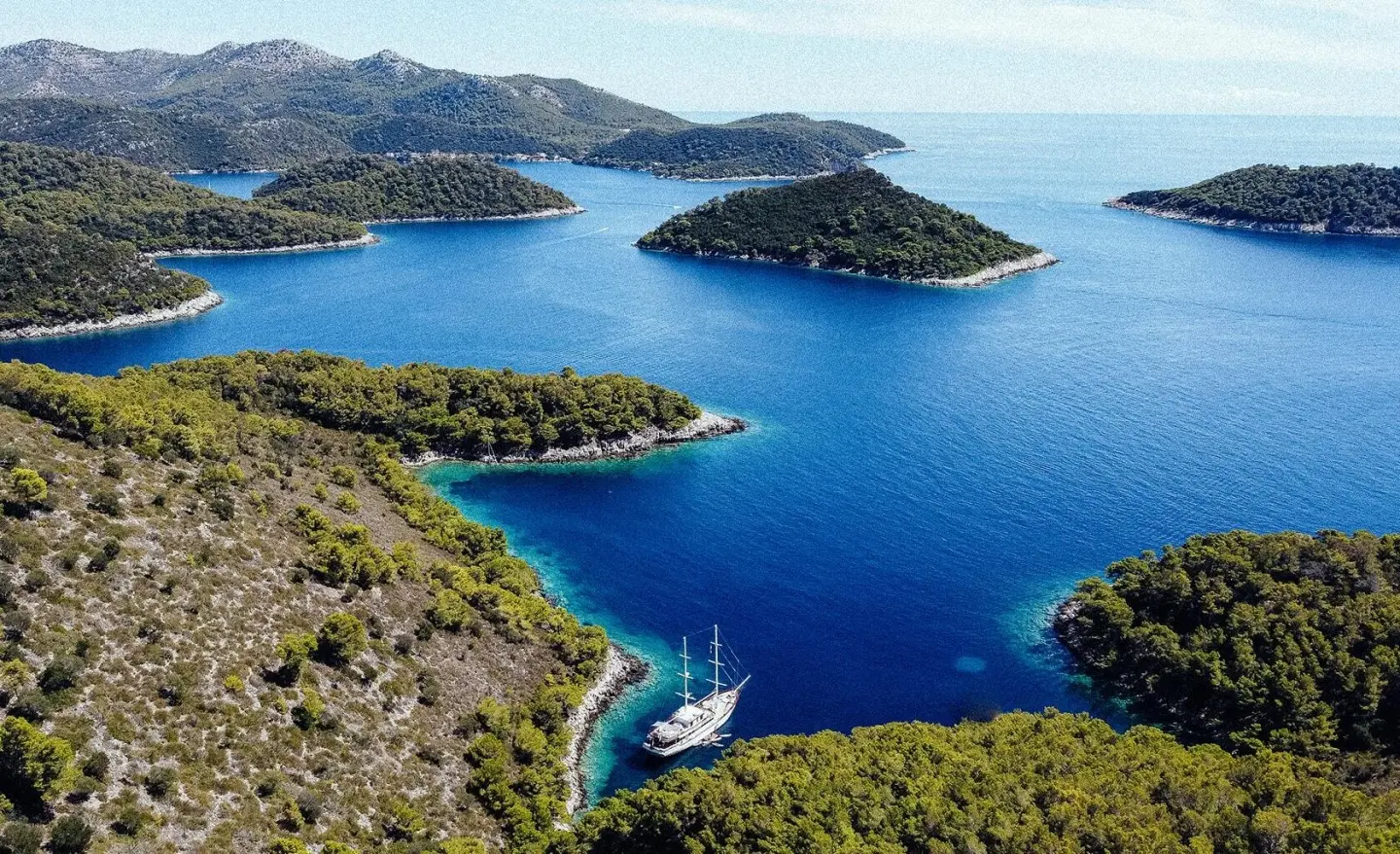 Gulet Corsario sails calm blue bay coastlines from aerial view yacht