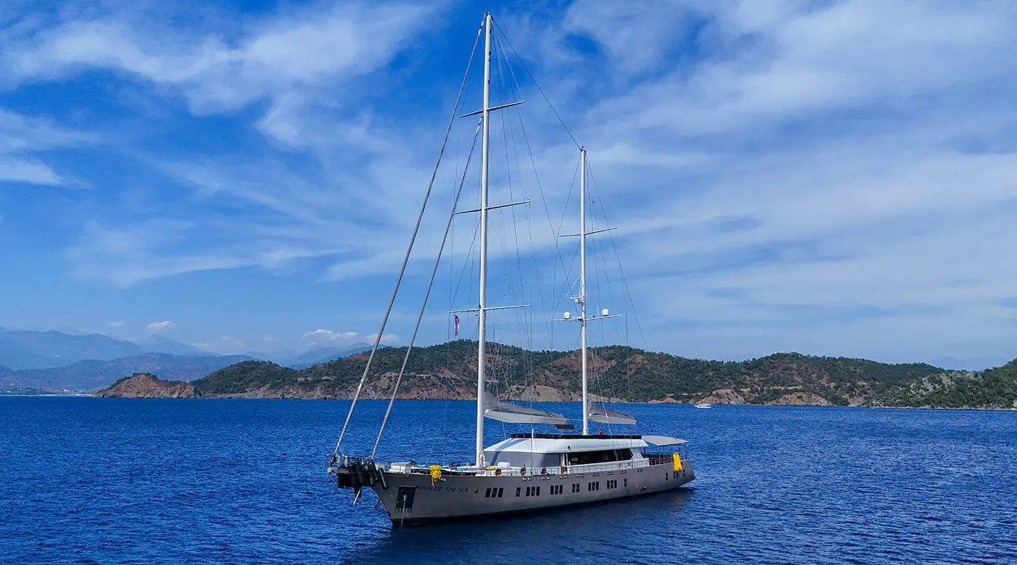 Sailboat yacht named King Of The Sea anchored in blue ocean with hill backdrop