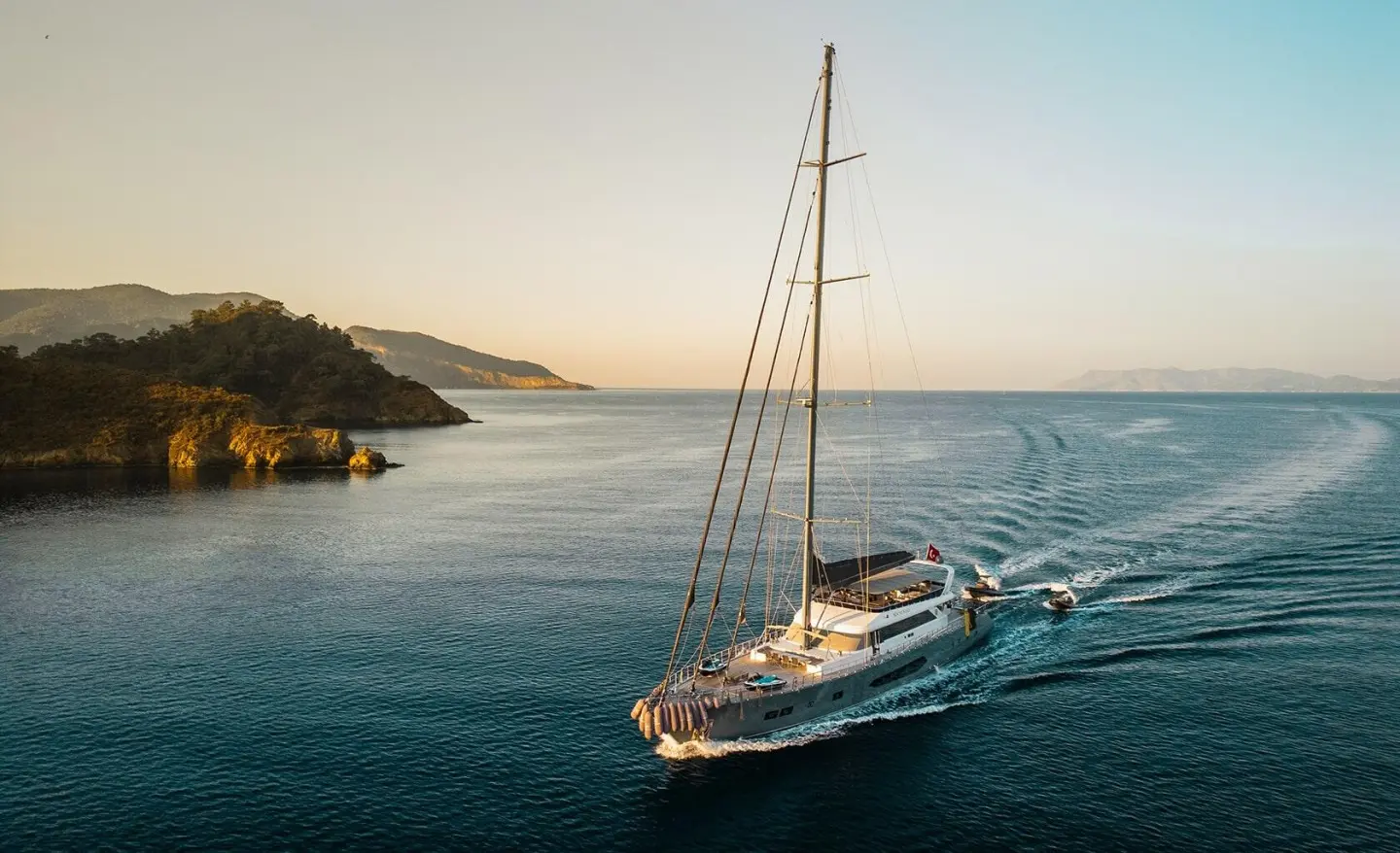 North Wind sailing yacht anchored in calm blue water near rocky coast at sunset