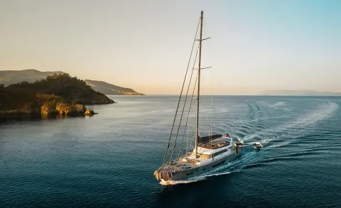 North Wind sailing yacht anchored in calm blue water near rocky coast at sunset