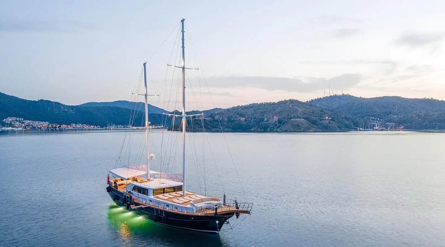 Gulet yacht named Happy Days anchored calmly on blue water with hills in background