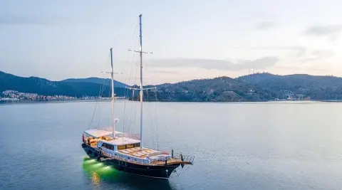 Gulet yacht named Happy Days anchored calmly on blue water with hills in background