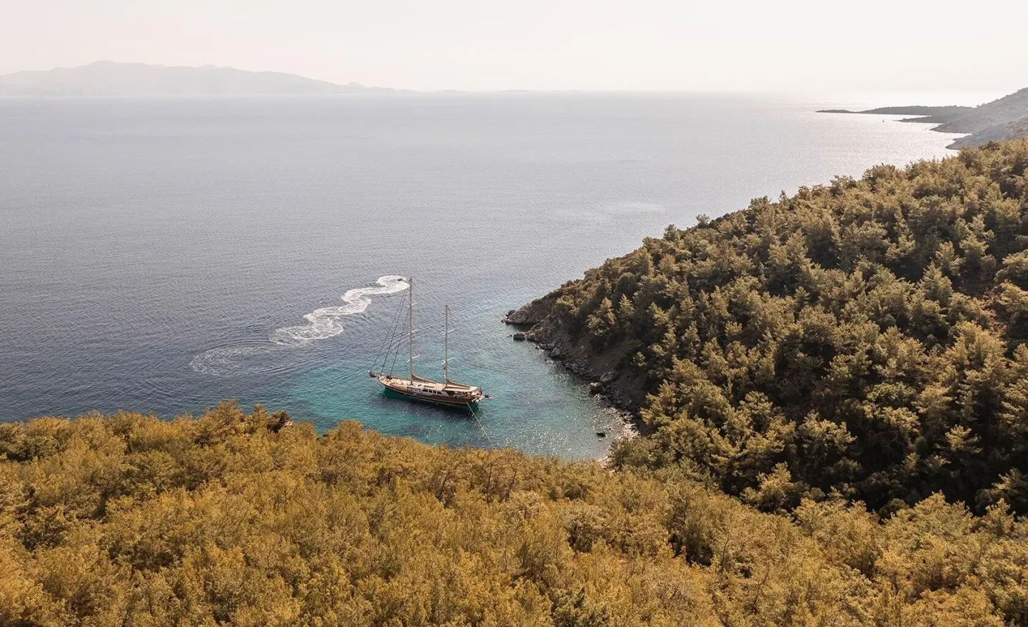 La Bella Vita gulet anchored offshore with rocky cliffs and calm blue sea