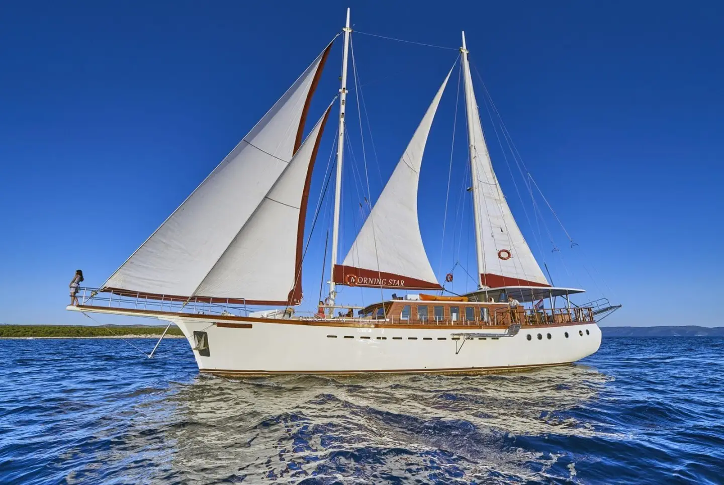 Sailing yacht Morning Star with white sails on blue sea and deck passengers