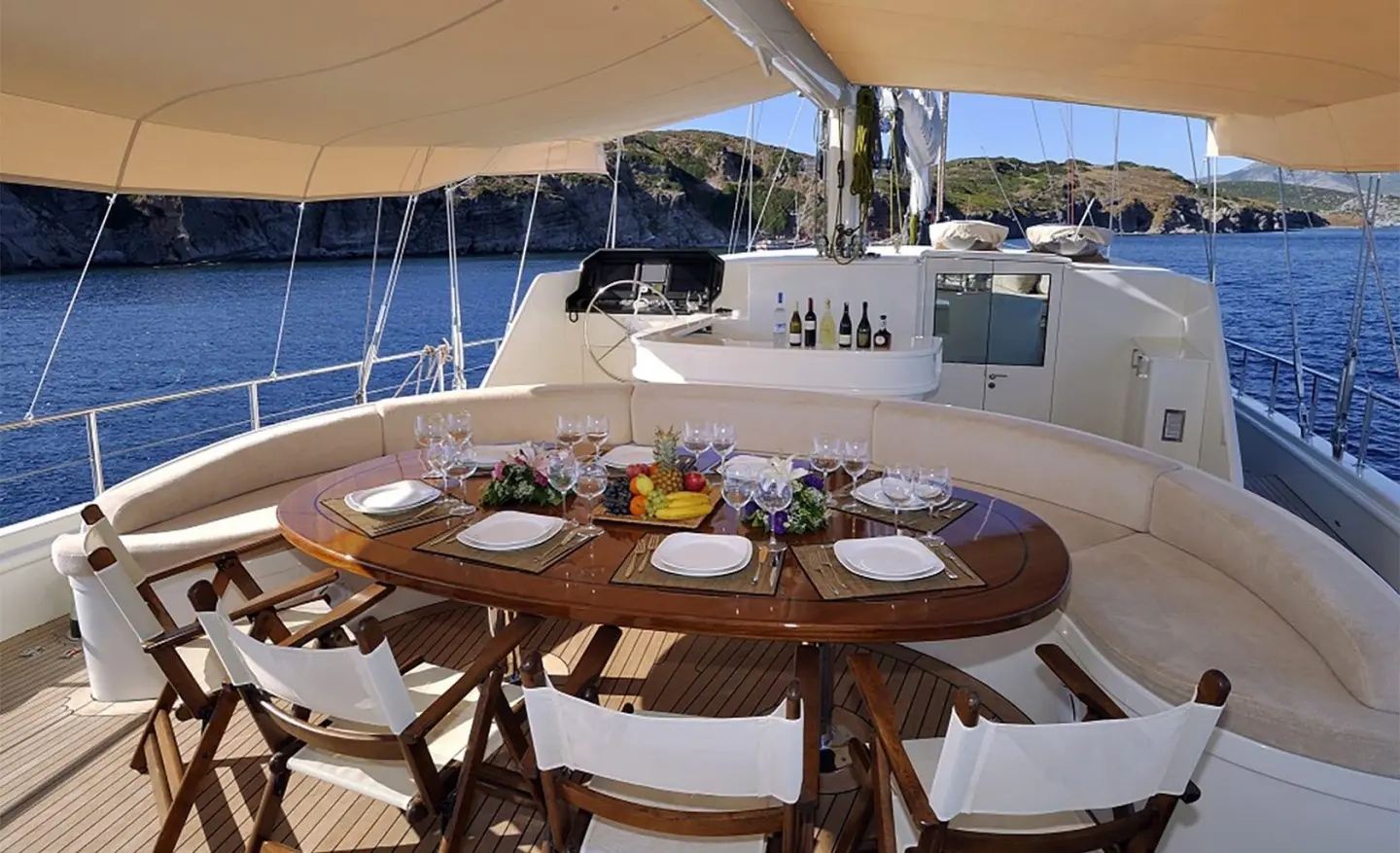 Dolce Mare yacht deck with wooden table, chairs, and sunlit seating area at sunset