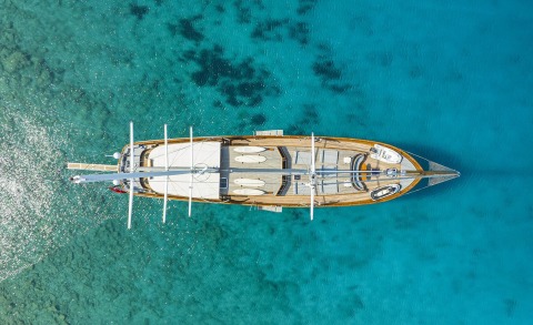 Top-down view of a brown wooden sailing yacht on blue water