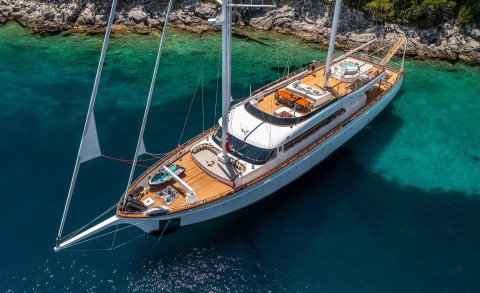 Love Story yacht seen from above in turquoise water by rocky shore with wooden deck and white hull