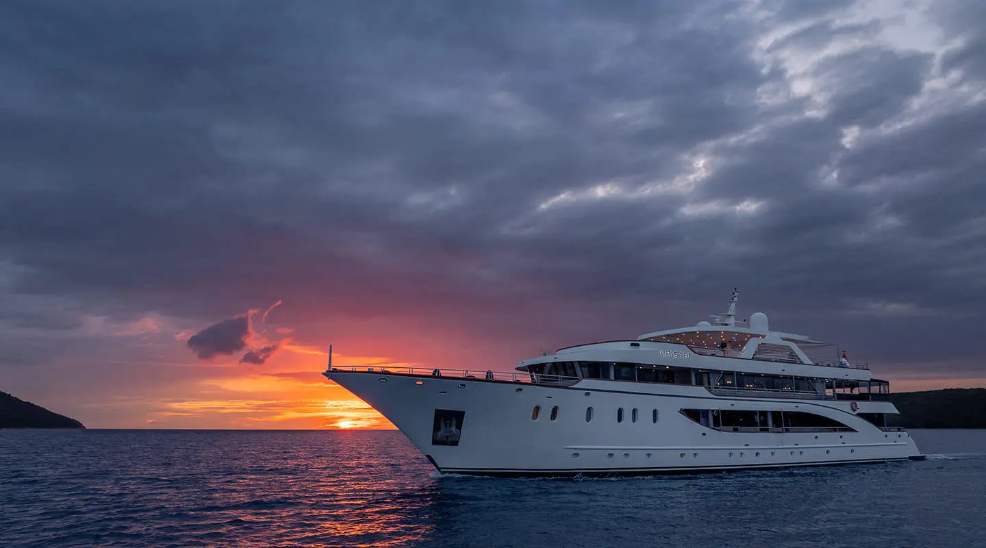 Motor yacht Cristal anchored at sunset with calm ocean and cloudy sky