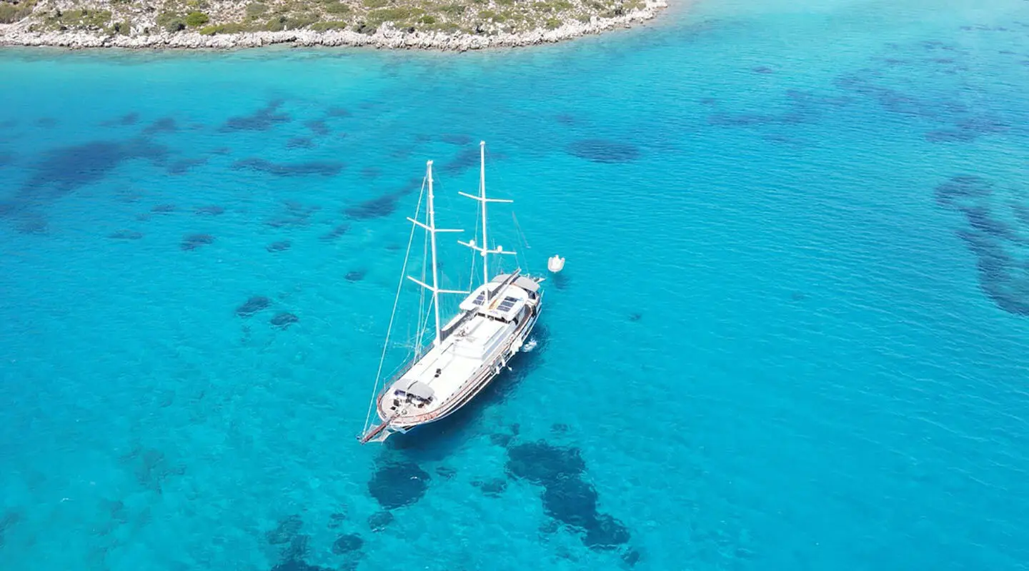 A sleek white yacht anchored in turquoise clear water near a rocky shoreline