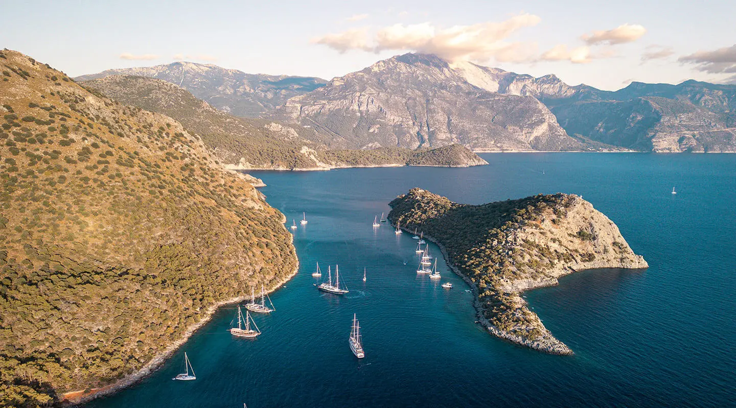 Queen Of Makri yacht anchored in a rocky cove at sunset with boats nearby