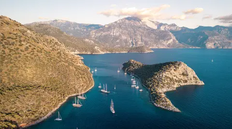 Queen Of Makri yacht anchored in a rocky cove at sunset with boats nearby