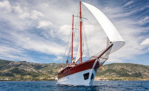 Romanca sailing yacht with white hull and red wood superstructure under a blue sky