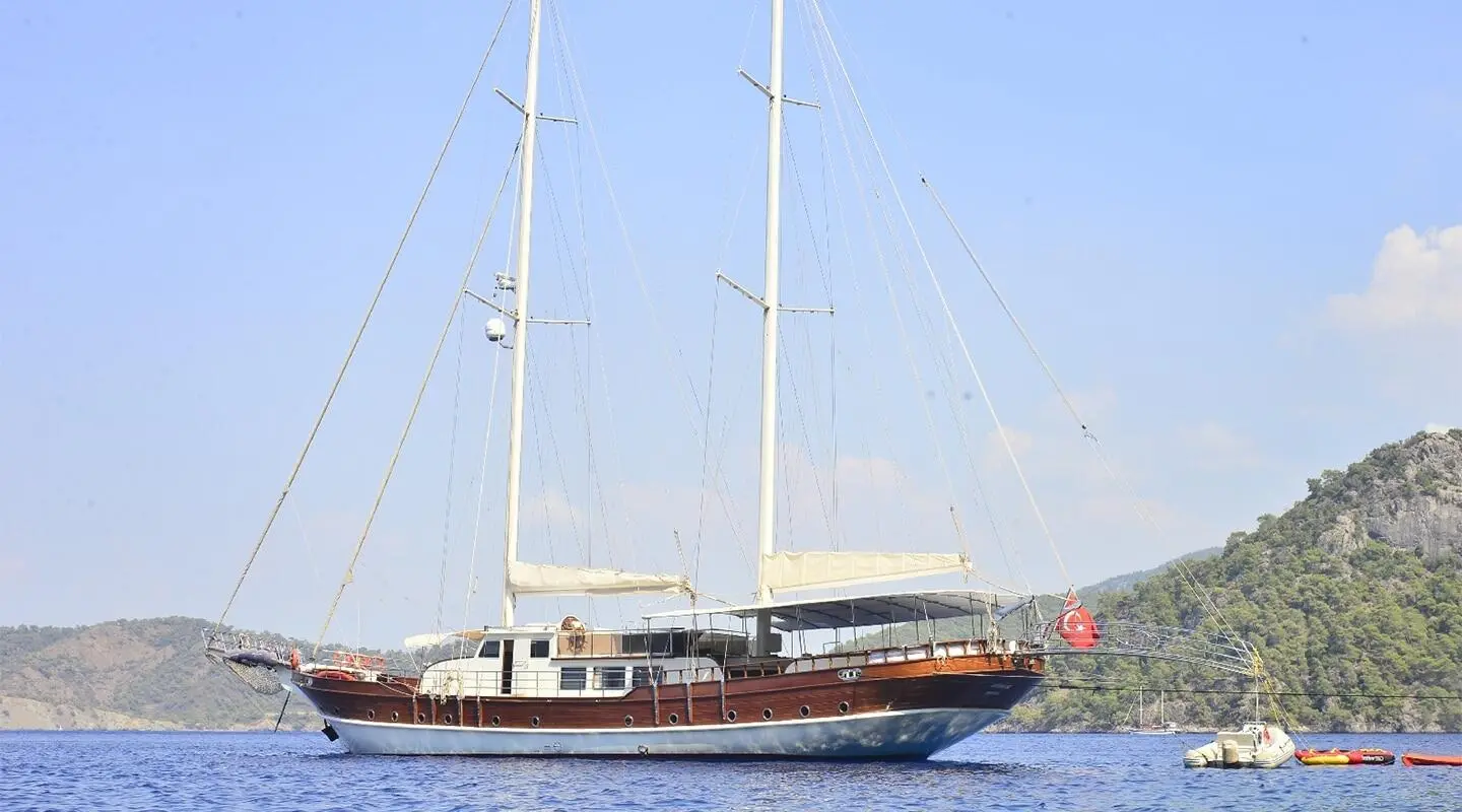 Yacht Berrak Su sailing boat with tall masts on calm blue water at sunset