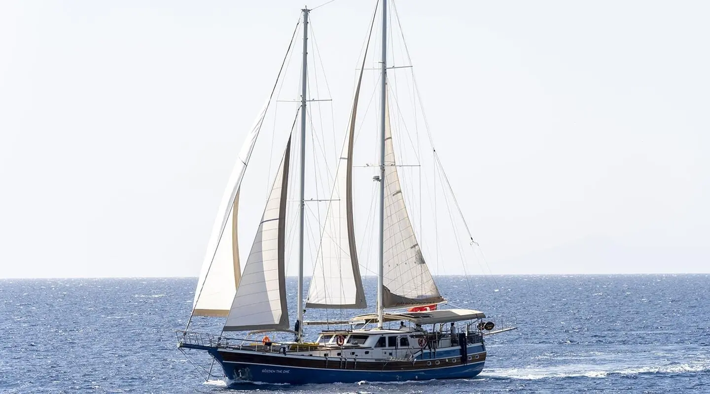 Gulet-style sailing yacht with blue hull on open sea and sails up