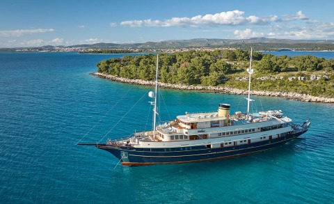 Luxurious Casablanca yacht anchored in blue water near a tree-covered island and distant shoreline