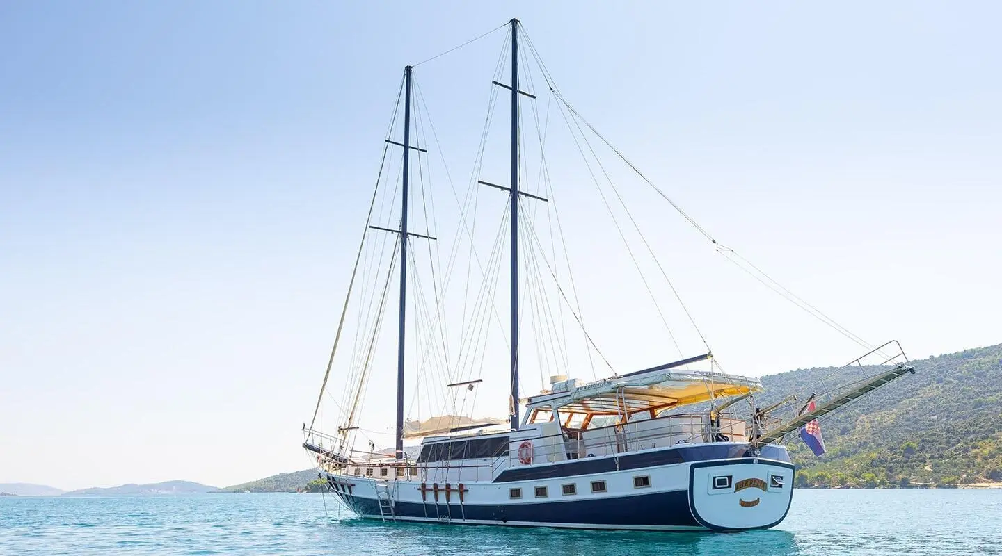 Two-masted gulet yacht anchored in calm blue-green water with sails down