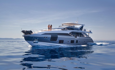 Two people sunbathing on the yacht's open deck with blue sea and sky in the background